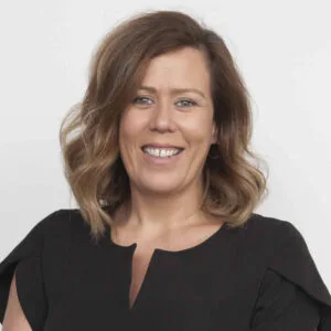 Professional headshot of a smiling woman, Skye Brodie, with wavy, shoulder-length brown hair, wearing a black dress.